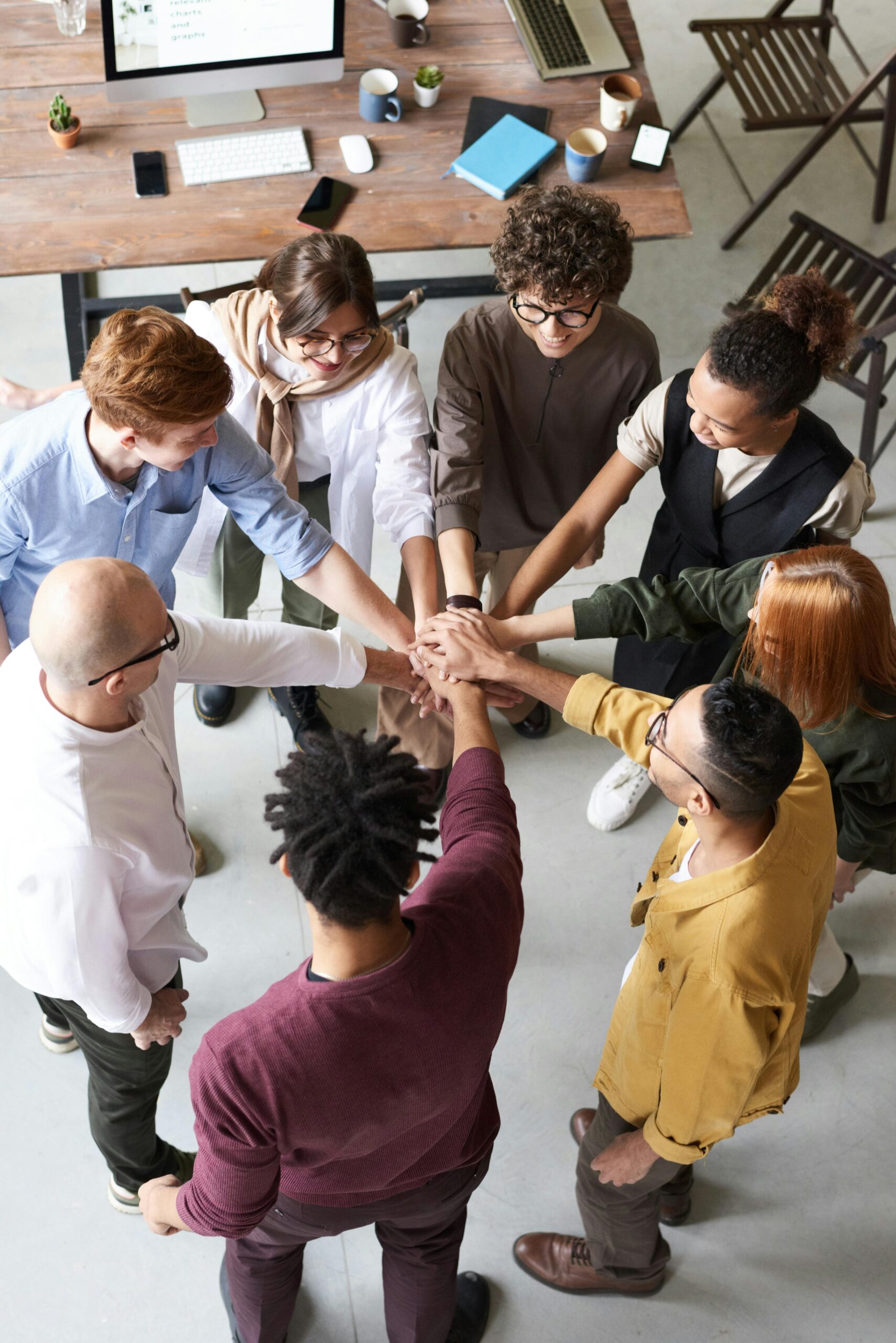 A diverse group of professionals joins hands in a team-building exercise indoors.